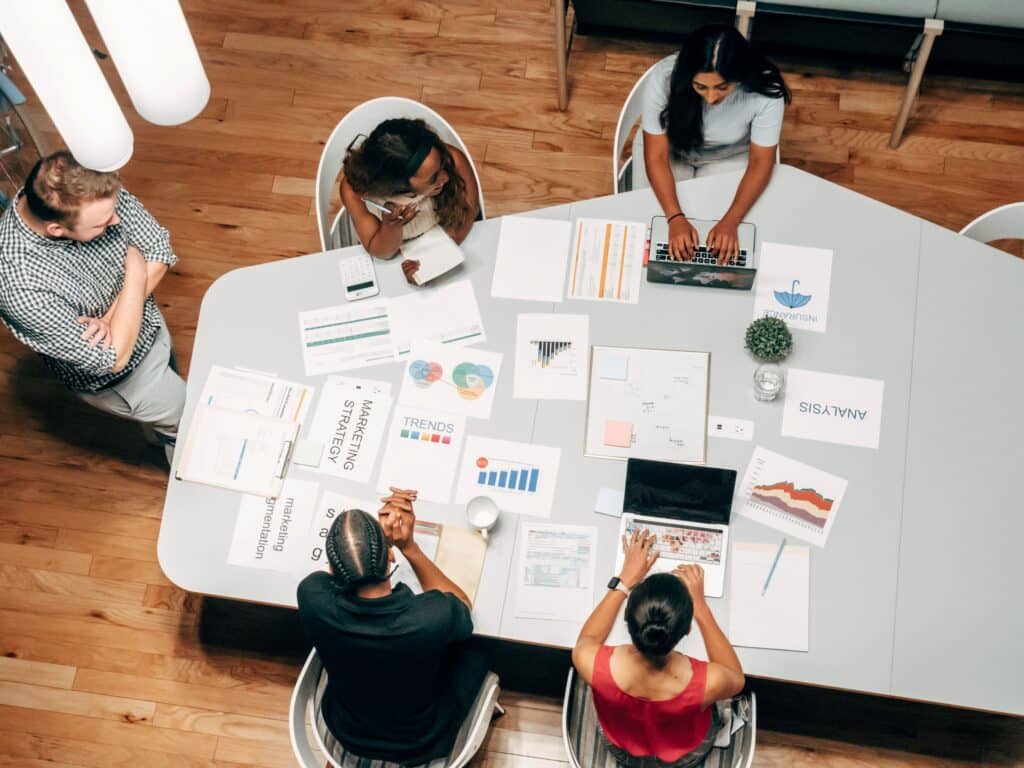 Bovenaanzicht van marketeers aan een bureau met een open laptop, aantekeningen en een koffiekopje